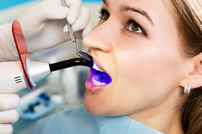 A woman receiving dental treatment, with a dentist using a device to clean or treat her teeth.