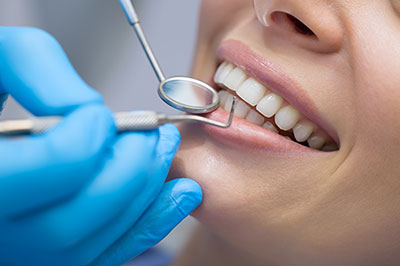 A dental professional using a drill on a patient s teeth, with the patient smiling and receiving treatment.