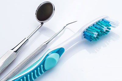 The image shows a collection of dental tools, including a pair of blue toothbrushes and various other implements typically found in a dental office, displayed on a white background.