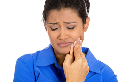 Woman in blue shirt, looking down with hand on her mouth, wearing a ring.