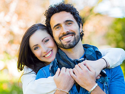 A man and a woman smiling at the camera, with the man wearing a blue t-shirt.