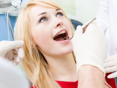 The image shows a young woman with her mouth open, receiving dental care from a professional in a clinical setting.