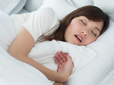 A woman is lying in bed, her eyes are closed and she appears to be asleep with a pillow under her head.