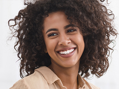 A smiling woman with curly hair, wearing a light-colored top and earrings, against a white background.